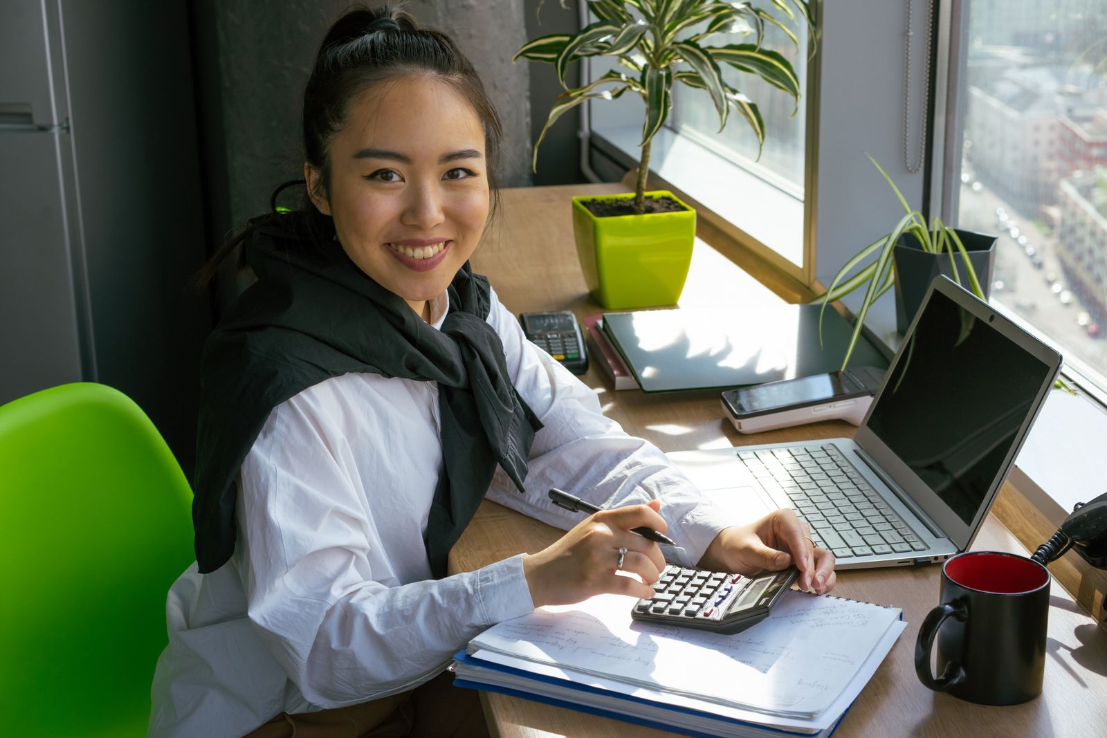 Nonprofit accountant reviewing books and printed reports at a bright office desk.