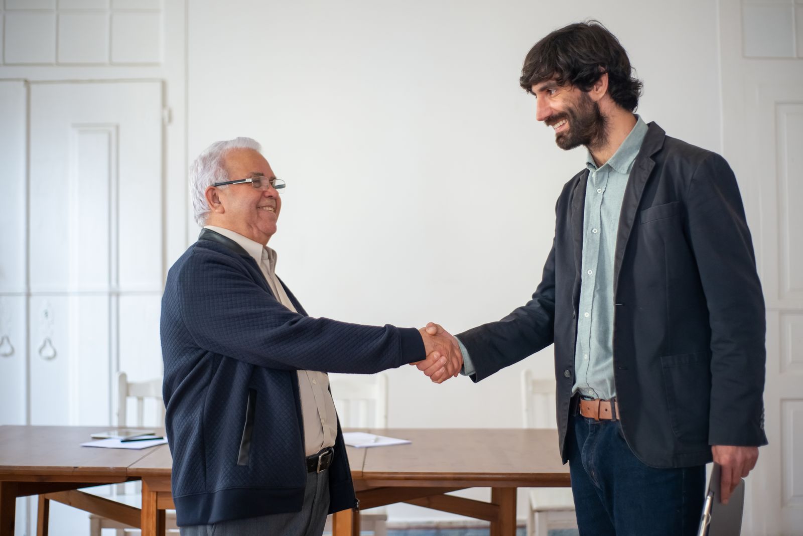 Senior consultant handing off a project to an incoming team member with a warm handshake.