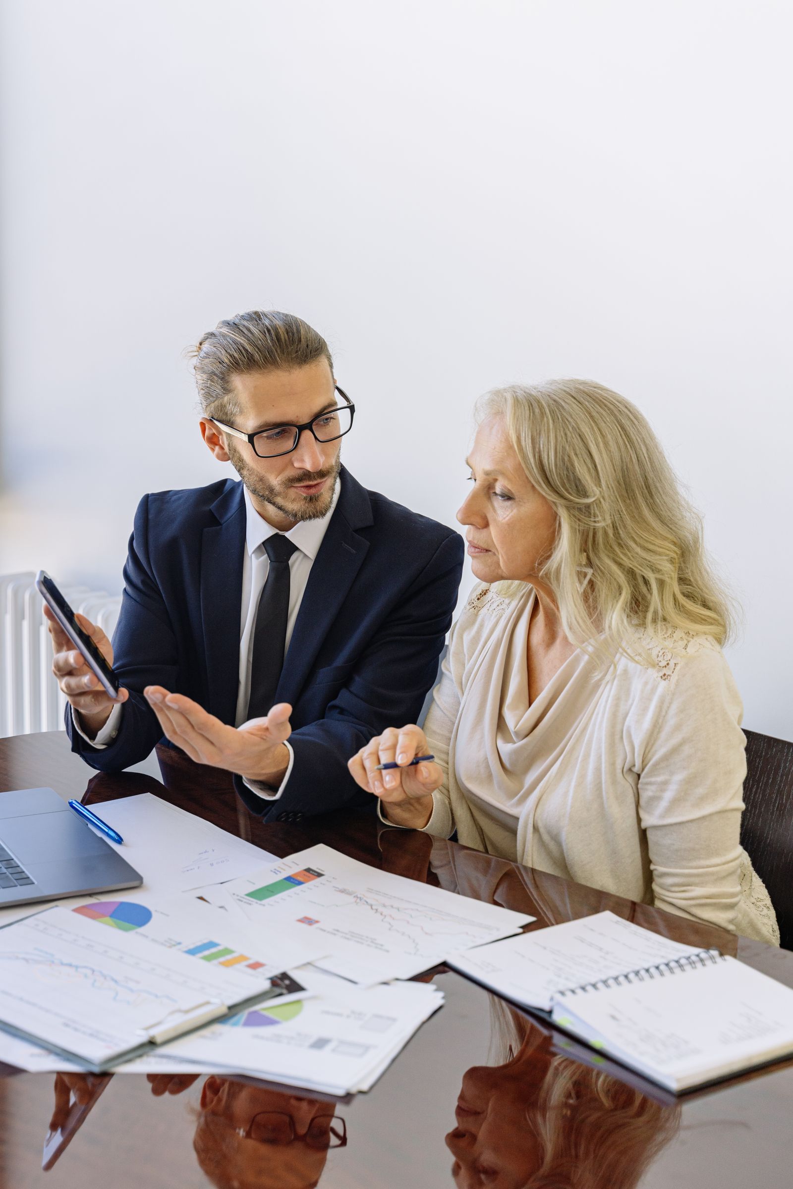 Advisor and executive reviewing printed financial charts across a conference table.