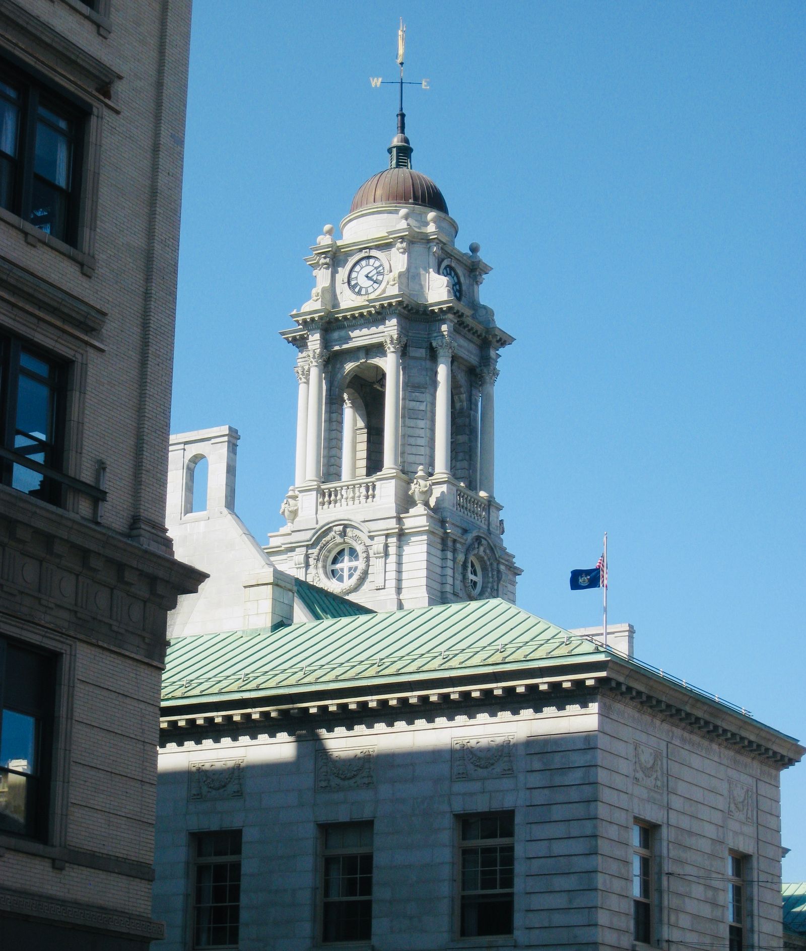 US city hall building with clock tower and American flag against a clear sky.