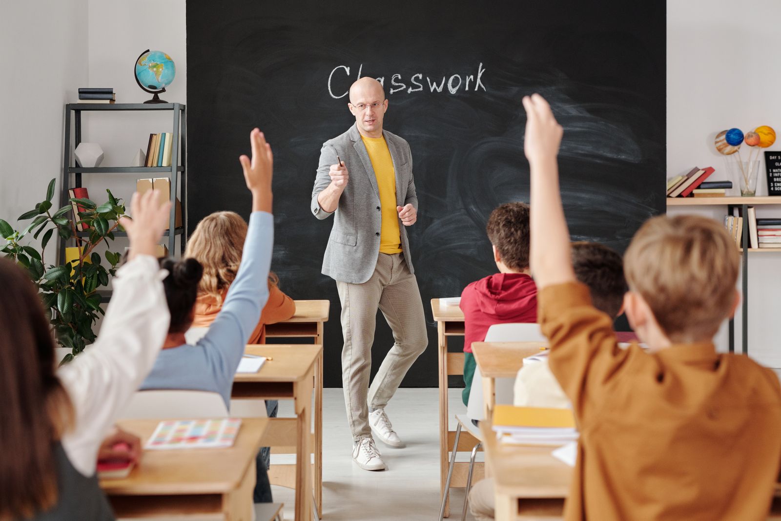 Teacher engaging students who are raising hands in a classroom.