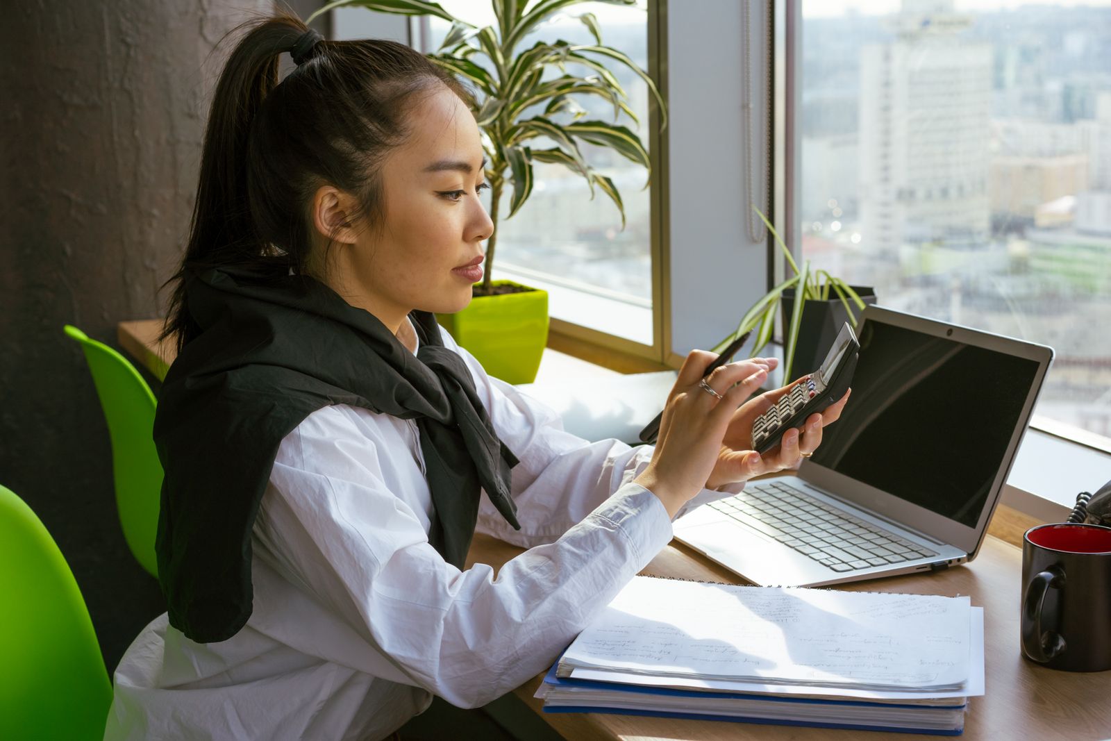 Accountant reviewing financial reports and spreadsheets on a laptop at a bright desk.